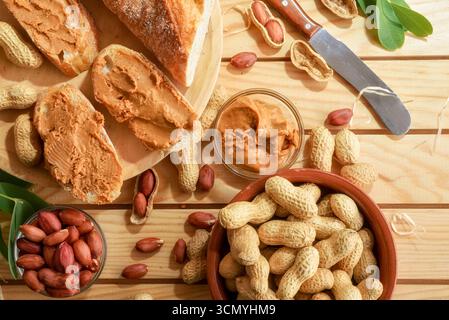 Freshly harvested homemade peanut butter and slices of bread on a wooden table with fruit outside in the sun. Top view. Stock Photo