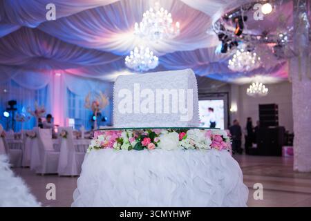 A beautifully arranged wedding money box sits atop a flower-adorned pedestal, surrounded by refined reception decor. Soft lighting enhances the romant Stock Photo