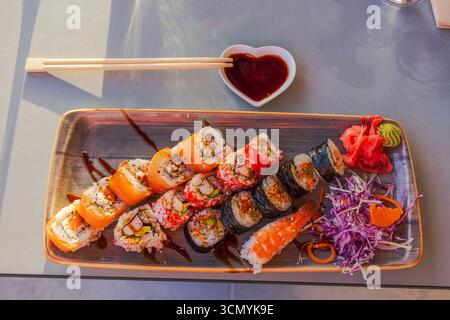 Close up view of assorted sushi rolls with shrimp and vegetables served on plate with soy sauce in heart bowl. Curacao. Stock Photo