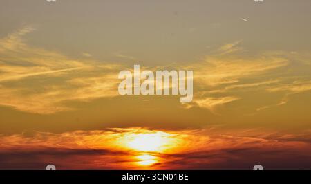 Magical twilight sky with fire-red and ash-gray tones as sunlight hides behind textured storm clouds in dramatic contrast. Stock Photo