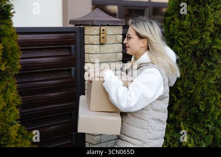 Courier delivering two cardboard boxes in front of a residential house gate, fulfilling ecommerce orders for customers in the neighborhood Stock Photo