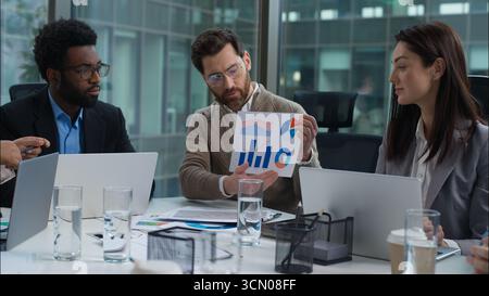 Caucasian leader manager showing graph chart employers coworkers team business woman African men male female in office briefing discuss statistics Stock Photo