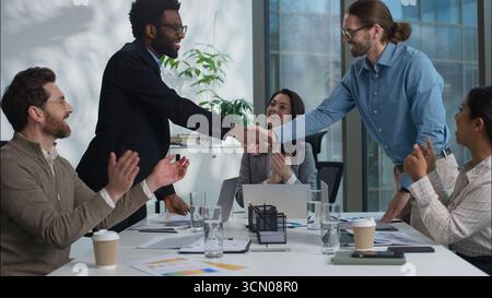 African American and Caucasian business men shaking hands partnership successful deal multiethnic office workers businesspeople women clapping Stock Photo
