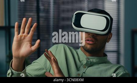 Scared worried african american man wearing virtual reality glasses playing scary 3d game in digital metaverse world indoors feel fear horror afraid Stock Photo
