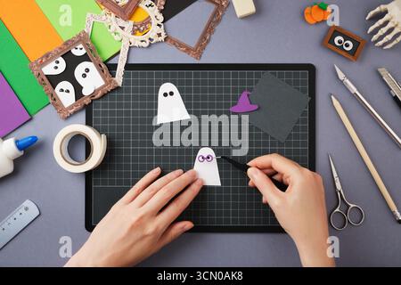 Making a Halloween craft. Hands glue the glasses to the ghost figure. Stock Photo