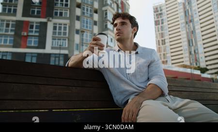 Caucasian European man sitting on bench male holding cup coffee break drinking takeaway order customer buyer relax tasty drink guy student businessman Stock Photo