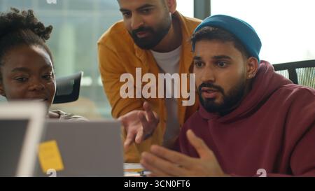 Three diversity colleagues workers in casual office arguing about document data looking in laptop multiracial informal small business team emotional Stock Photo