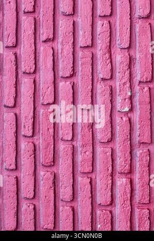 Vertical pink red brick wall with uniform pattern, rough texture, and visible mortar lines, creating a rustic abstract design background. Stock Photo