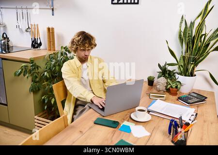 A young man in casual attire engages with his laptop at a stylish home workspace filled with plants. Stock Photo