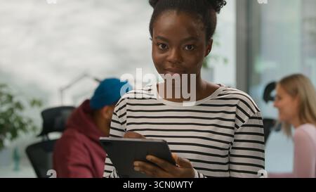 Portrait African American casual businesswoman typing digital tablet online app looking at camera smiling informal business woman female girl in Stock Photo