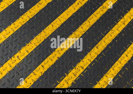 Industrial black and yellow diagonal stripes painted on a metal surface with a non-slip tread pattern. Represents safety, caution, and industrial desi Stock Photo