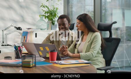 Two multiethnic business people informal team in office working laptop talking African American businessman Hindu businesswoman looking computer Stock Photo