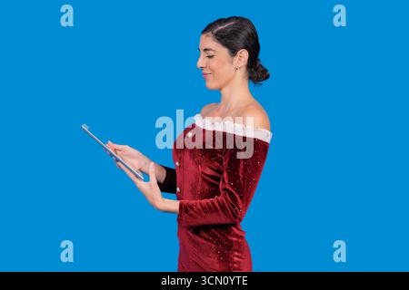 Woman in a red velvet dress smiling, viewing digital content on a tablet Stock Photo