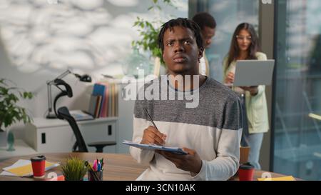Concentrated African American business man pondering writing notes businessman male guy working in informal creative startup office near diversity Stock Photo