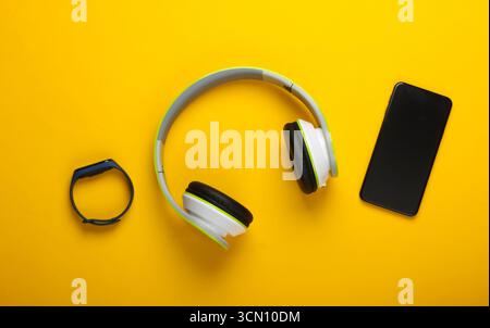 Flat lay composition of modern gadgets. Wireless headphones, smart bracelet, smartphone on yellow background. Millennial stuff. Top view Stock Photo