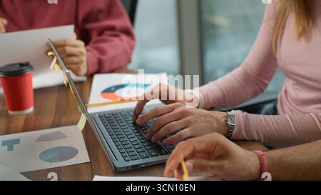 Three unrecognizable colleagues typing laptop paperwork unknown group business team informal workers using computer businesswoman cooperating with two Stock Photo