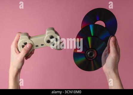 Hands hold cd discs and gamepad on pink pastel background. Gaming, recreation and entertainment Stock Photo