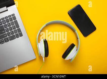 Laptop with stereo headphones and smartphone on yellow background. Flat lay composition. Modern gadgets. Top view Stock Photo