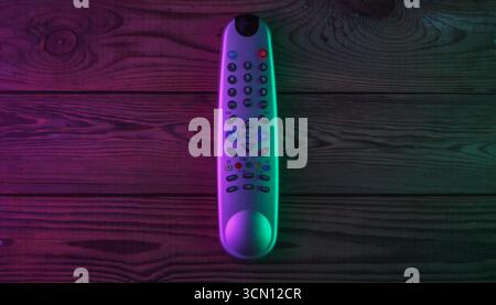 Tv remote on wooden background with green magenta neon light. Top view Stock Photo
