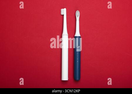 Two Modern electric toothbrushes on red background. Top view. Teeth care. Minimalism Stock Photo