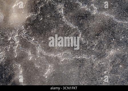 Macro of thin ice with subtle traces of air bubbles, faint stones visible underneath, showing delicate textures on Norwegian coast in winter Stock Photo