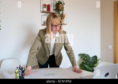 Woman architect analyzing blueprint in home office Stock Photo