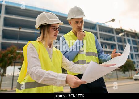 Engineers discussing blueprints at construction site Stock Photo