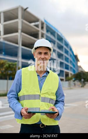 Construction engineer smiling wearing hard hat holding tablet Stock Photo