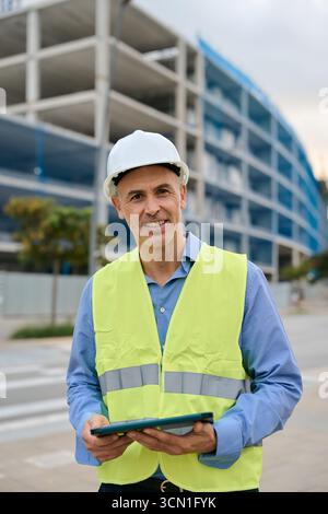 Smiling engineer supervising construction site holding tablet Stock Photo