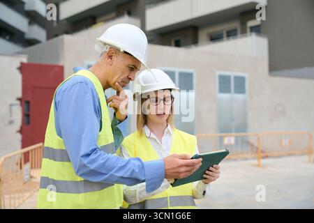 Engineers reviewing construction plans on tablet at building site Stock Photo