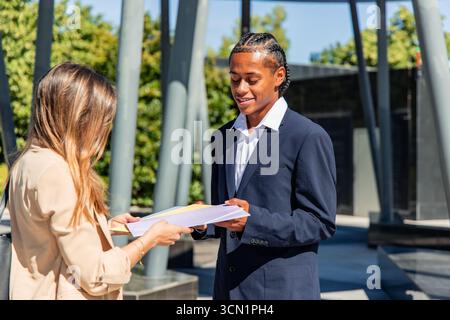multicultural Business partners exchanging documents in the vibrant financial district, illustrating a successful collaboration and strong agreement b Stock Photo