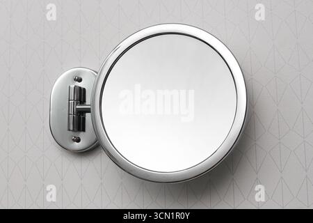 Round wall mounted mirror. Bathroom interior detail closeup. Modern accessory with chrome frame. Reflection object on tiled wall. Stock Photo