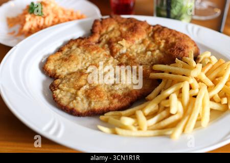 Plate with schnitzel and french fries. Traditional fried meat dish served with salad. Delicious lunch meal on table. Tasty fast food concept. Stock Photo