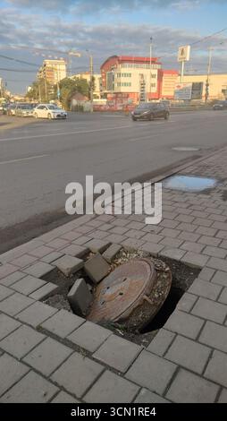 collapsed manhole, unmarked, on a sidewalk next to a busy street, a real danger for pedestrians, in the city of Iasi, Romania Stock Photo