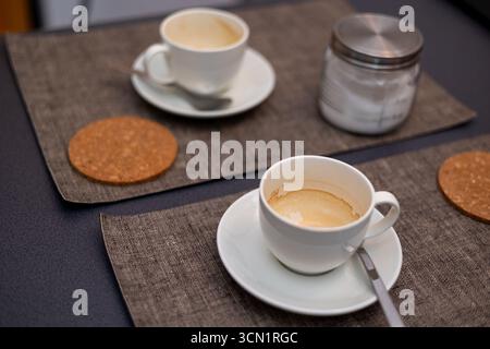 Used white coffee cups with coffee residue and cork coasters on wooden table in cafe setting Stock Photo