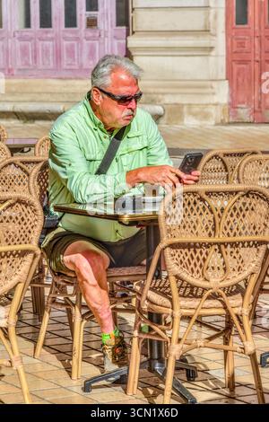 Man with sunglasses sat at outdoor cafe table looking at smartphone - Tours, Indre-et-Loire (37), France. Stock Photo