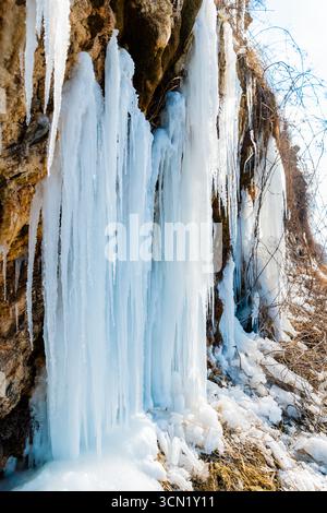 Crystal frozen waterfall with long icicles on a rocky cliff in winter. Stock Photo