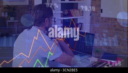 Analyzing middle-aged man using laptop in home office, with financial charts and potted succulent. Technology, productivity, modern, workspace, intell Stock Photo