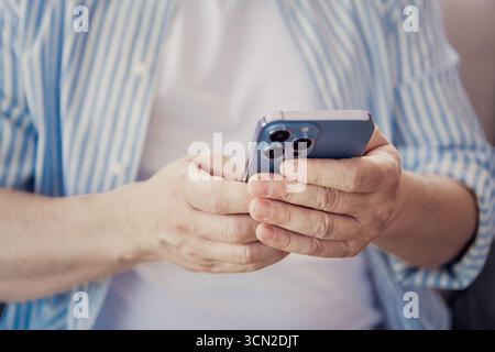 Mature individual using a smartphone indoors, demonstrating mobile technology, casual lifestyle, and modern connectivity Stock Photo