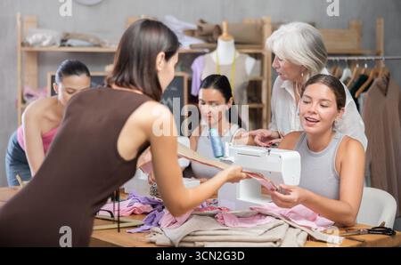 In sewing class young woman working on machine and discussing pattern Stock Photo