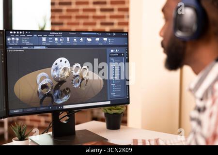 African american male engineer seated at home desk, developing digital prototypes using computer aided design tools. Creative developer focused on construction innovation and 3D modeling workflow. Stock Photo