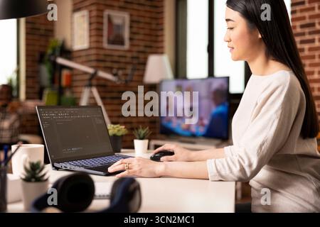 Remote software developer working on laptop, typing in programming language for startup project. Young female IT expert seated at desk, managing web development from cozy home. Stock Photo