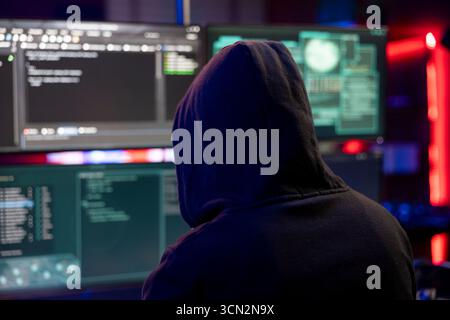 Hacker doing covert operations in hideout to bypass advanced security barriers. Cybercriminal in neon apartment engineering data theft script to penetrate firewalls using PC Stock Photo