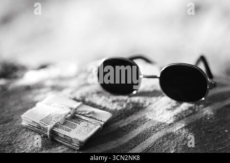 Vintage sunglasses and a stack of papers on a striped surface. Black and white photograph showcases a pair of round sunglasses next to a bundled stack Stock Photo