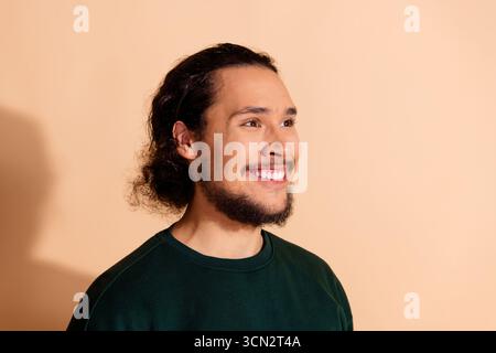 Portrait of a cheerful young man with a beard wearing a green sweatshirt on a beige background Stock Photo