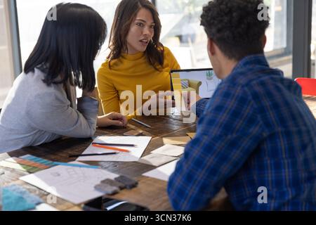 Diverse design professionals collaborating at table in office with tablet with swatches sketches Stock Photo