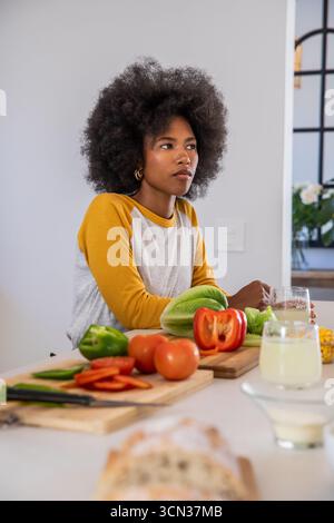 African american woman slicing vegetables on cutting boards at kitchen counter with bread and drink Stock Photo