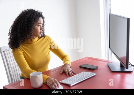 African american woman typing on keyboard at desk with monitor in home office, copy space Stock Photo