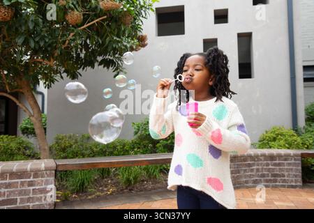 African american child in sweater blowing soap bubbles with pink wand and solution bottle Stock Photo