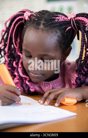 African american child leaning forward at study desk highlighting notes with highlighter Stock Photo
